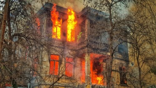 roaring flames coming out of the windows of a large house